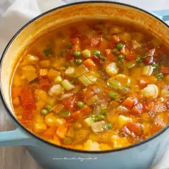 Un fumante minestrone di verdure in una casseruola azzurra, ricco di carote, zucchine, piselli e pomodoro.