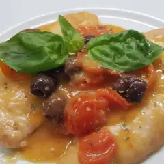 Delizioso pollo alla mediterranea con pomodorini, olive nere e basilico fresco su un piatto bianco.
