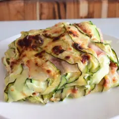 Una fetta di parmigiana di zucchine light, con strati di zucchine sottili, formaggio filante e prosciutto cotto, gratinata al forno.