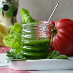 Un vasetto di salsa al basilico, con pomodoro, limone e lattuga sullo sfondo.
