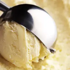Un cucchiaio raccoglie una pallina di cremoso gelato fatto in casa, dal colore giallo pallido e dalla consistenza invitante.