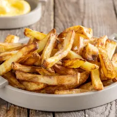 Patate in friggitrice ad aria, dorate e croccanti, servite in una ciotola su un tavolo di legno.