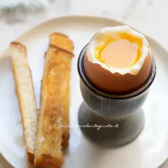 Un delizioso uovo alla coque con tuorlo dorato, servito con croccanti bastoncini di pane tostato.