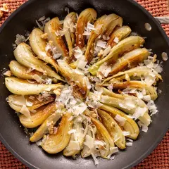 Finocchi in padella dorati, guarniti con scaglie di formaggio e noci croccanti. Un piatto semplice e gustoso.
