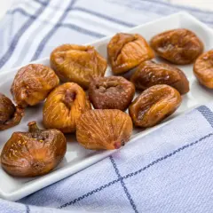 Fichi secchi al forno, caramellati e lucidi, disposti su un piatto bianco, con un tovagliolo a quadri blu e bianchi.