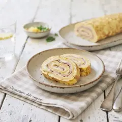 Delizioso rotolo di frittata con prosciutto e formaggio, servito su un piatto con una forchetta e un coltello.