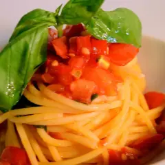 Spaghetti conditi con un fresco sugo con pomodorini freschi e basilico, un piatto semplice e gustoso.