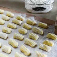 Gnocchi di patate ricetta: tanti piccoli gnocchi fatti in casa, pronti per essere cotti. Sullo sfondo, farina e un attrezzo per rigarli.
