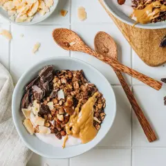 Una ciotola di granola fatta in casa con yogurt, burro di arachidi, scaglie di cocco e pezzi di cioccolato fondente.