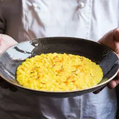Chef presenta un cremoso risotto alla milanese, dorato e profumato, guarnito con fili di zafferano.