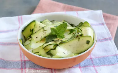 Insalata di zucchine marinate, condite con erbe aromatiche e menta fresca, servite in una ciotola di terracotta.