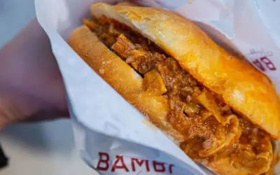Panino con trippa alla fiorentina, un classico street food toscano, avvolto in carta con logo.