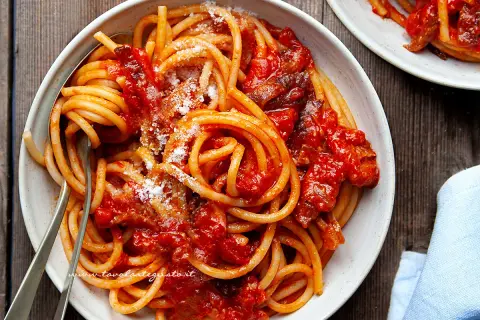 Un piatto invitante di bucatini all'amatriciana ricetta, conditi con sugo rosso e guanciale croccante, spolverati di pecorino.