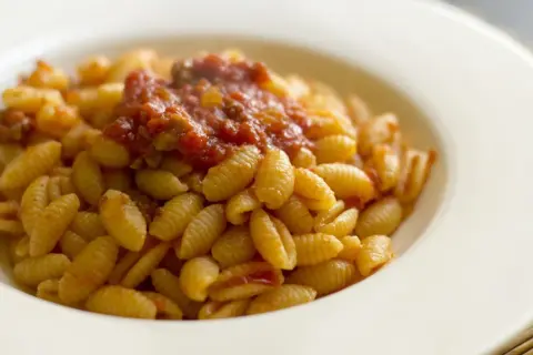 Un piatto di malloreddus alla campidanese, pasta sarda con sugo di pomodoro e salsiccia, serviti in una ciotola bianca.
