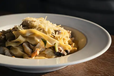 Un piatto di pasta fresca con salsiccia e funghi, condita con parmigiano grattugiato.