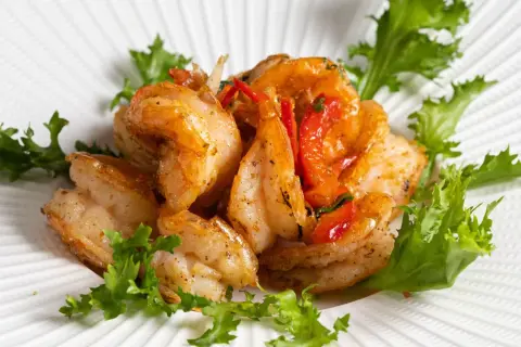 Gamberi sale e pepe succulenti, saltati con pomodorini e guarniti con insalata fresca su un piatto bianco texturizzato.