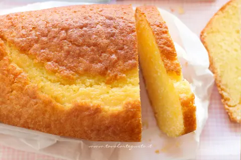 Un soffice plumcake allo yogurt, dorato e invitante, con una fetta tagliata che ne mostra la morbidezza. Perfetto per la colazione.