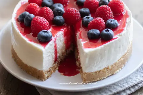 Cheesecake con mascarpone, guarnita con lamponi e mirtilli freschi, con una colata di salsa rossa.