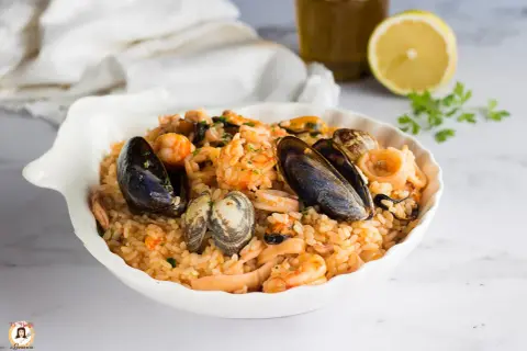 Un invitante risotto allo scoglio, ricco di cozze, vongole, gamberi e calamari, servito in una conchiglia bianca.