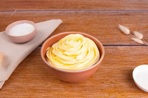 Una ciotola di soffice crema al burro, pronta per decorare torte. Accanto, ciotoline con zucchero e decorazioni naturali.