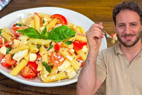 Un uomo sorride mentre assaggia una forchettata di pasta alla crudaiola, un piatto fresco con pomodorini, mozzarella e basilico.
