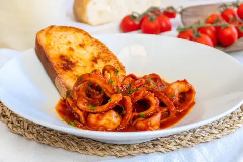 Un piatto di moscardini in umido, succulenti e profumati, accompagnati da una fetta di pane tostato e pomodorini freschi.