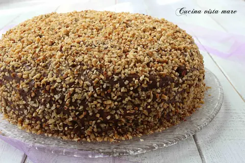 Torta ricoperta di cioccolato e nocciole tritate, una deliziosa pizza dolce abruzzese su un piatto di vetro.