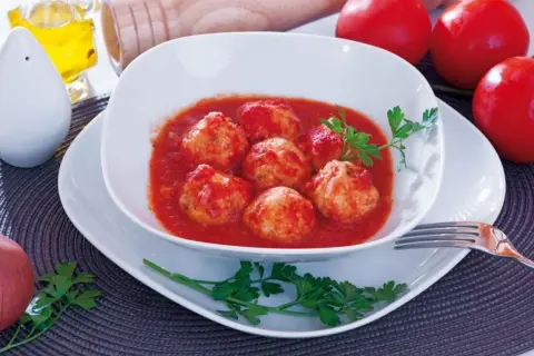 Polpette di merluzzo in salsa di pomodoro, guarnite con prezzemolo. Sullo sfondo, pomodori, cipolla e sale.
