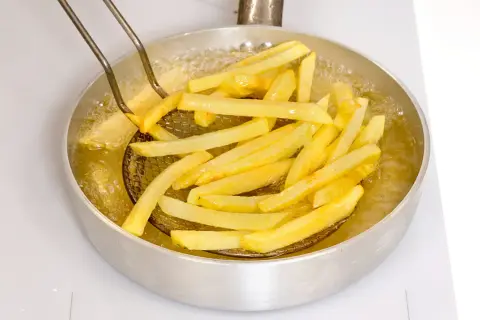 Patatine fritte dorate che sfrigolano nell'olio bollente, pronte per essere gustate.