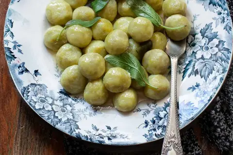 Un piatto di gnocchi di zucchine, conditi con burro e salvia, su un elegante piatto decorato.
