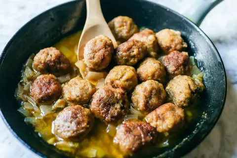 Polpette in bianco cremose in padella, dorate e succulente, adagiate su un letto di cipolle caramellate.