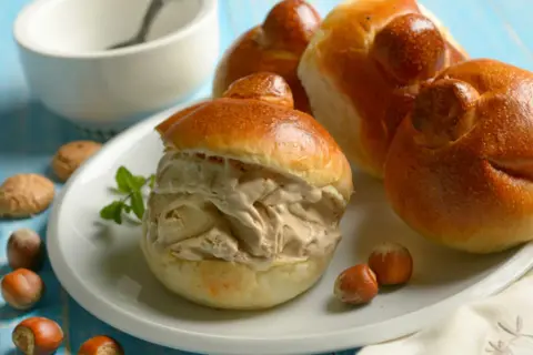 Brioche col tuppo ripieno di gelato, con nocciole e biscotti intorno.