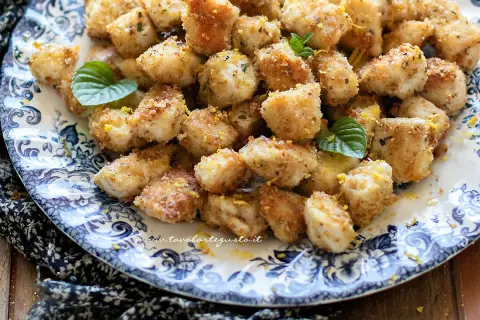 Bocconcini di pollo dorati e croccanti, guarniti con scorza di limone e foglioline di menta, serviti su un piatto decorato.