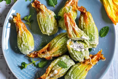 Fiori di zucca fritti, ripieni di formaggio cremoso e guarniti con menta fresca, su un piatto blu.