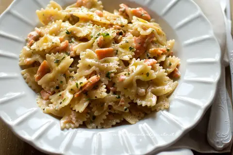 Farfalle cremose con salmone affumicato, un piatto delizioso e invitante, guarnito con prezzemolo fresco e pepe nero.