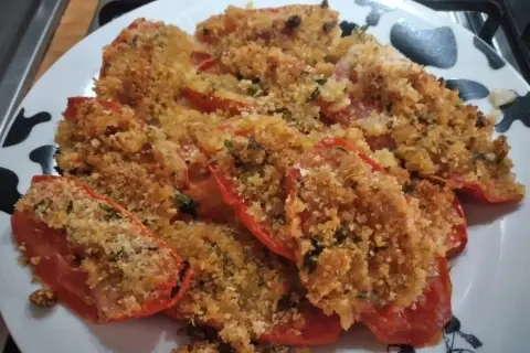 Pomodori al forno ripieni di pangrattato e erbe aromatiche, dorati e invitanti.