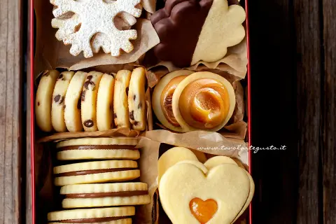 Scatola piena di biscotti al burro: a fiocco di neve, con gocce di cioccolato, ripieni di caramello e a forma di cuore.
