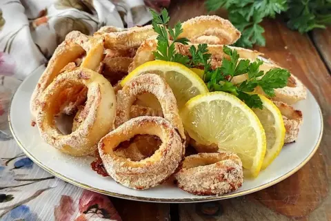 Anelli di calamari gratinati al forno, dorati e croccanti, guarniti con spicchi di limone e prezzemolo fresco.