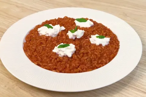 Un cremoso risotto al pomodoro, arricchito da ciuffi di ricotta fresca e basilico, servito su un piatto bianco.