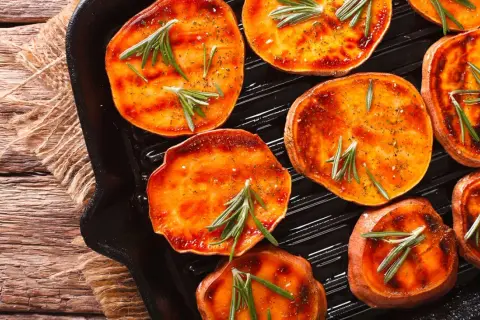 Fette di patate dolci grigliate in padella con rosmarino e spezie, pronte per essere gustate.