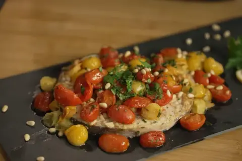 Pesce spada in friggitrice ad aria, condito con pomodorini colorati, pinoli e prezzemolo fresco. Un piatto leggero e saporito.