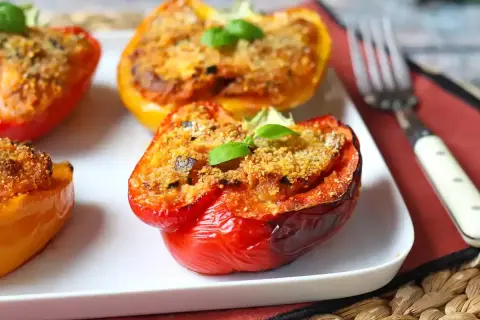 Peperoni ripieni al forno, colorati e invitanti, con un ripieno dorato e una fogliolina di basilico fresco.