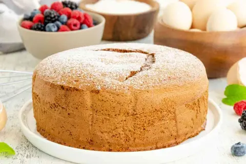 Una soffice torta margherita spolverata di zucchero a velo, pronta per essere gustata con frutti di bosco freschi.