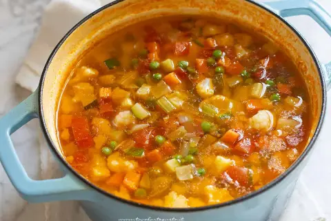 Un fumante minestrone di verdure in una casseruola azzurra, ricco di carote, zucchine, piselli e pomodoro.
