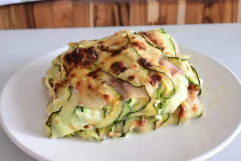 Una fetta di parmigiana di zucchine light, con strati di zucchine sottili, formaggio filante e prosciutto cotto, gratinata al forno.