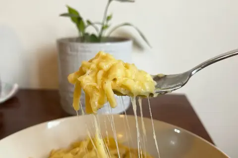 Un primo piatto cremoso: pasta e patate con provola filante, servita su una forchetta.