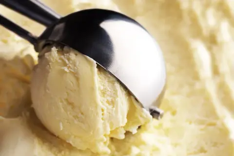 Un cucchiaio raccoglie una pallina di cremoso gelato fatto in casa, dal colore giallo pallido e dalla consistenza invitante.