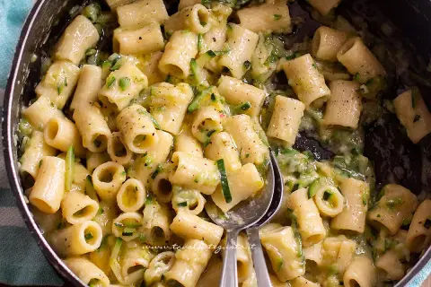 Close-up of rigatoni pasta with zucchini in a creamy sauce in a pot.