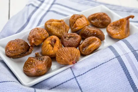 Fichi secchi al forno, caramellati e lucidi, disposti su un piatto bianco, con un tovagliolo a quadri blu e bianchi.
