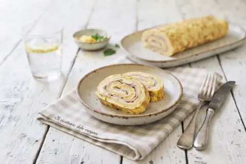 Delizioso rotolo di frittata con prosciutto e formaggio, servito su un piatto con una forchetta e un coltello.